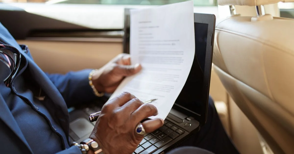 Un homme d'affaires examine des documents sur un ordinateur portable tout en voyageant à l'arrière d'une voiture.